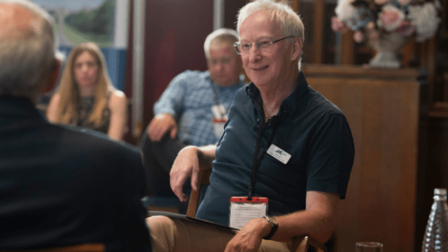 A smiling participant seated in a wood-panelled room during a programme session
