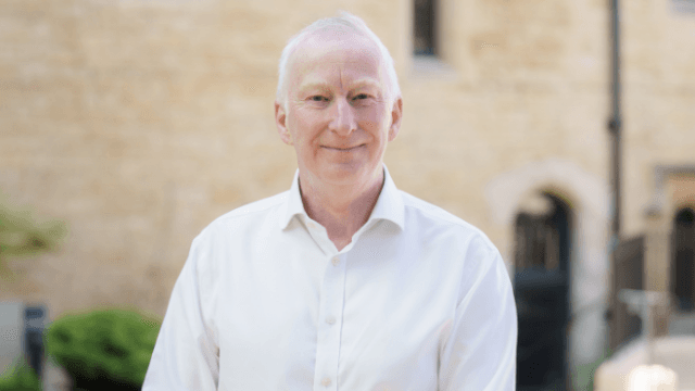 Dr Ed Newell, smiling, outside a stone building