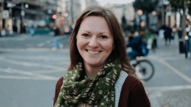 A smiling woman in a green scarf on a city street