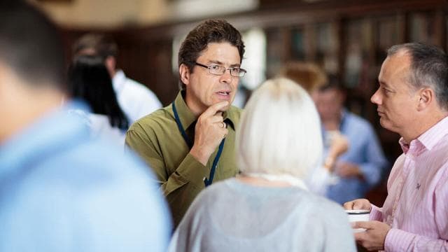 Participants from different organisations in conversation, one listening thoughtfully, hand to chin