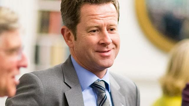 A senior leader in a suit smiles during a conversation