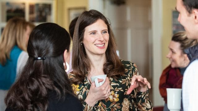 A smiling participant holding a cup of tea talks with colleagues during a break