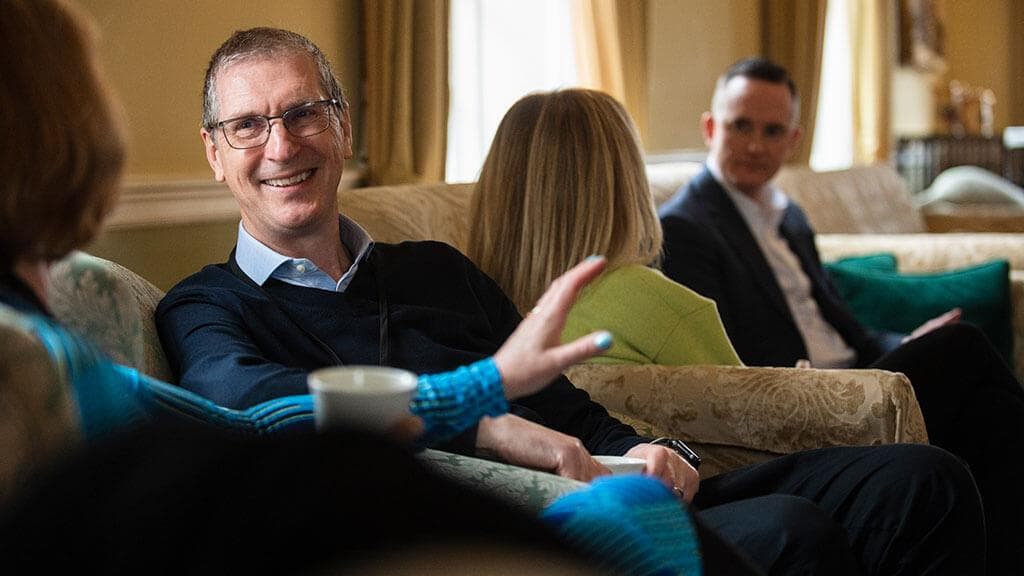 A smiling participant talks with colleagues in a lounge during a programme
